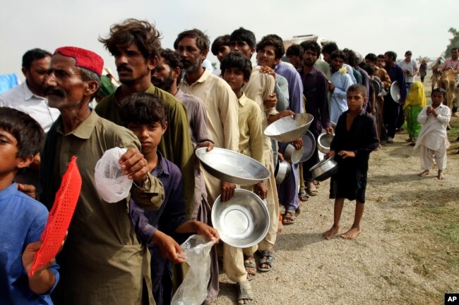 FILE - Flood affected people stand in a long line with utensils to get food distributed by Pakistani Army troops in a flood-hit area in Rajanpur, district of Punjab, Pakistan on August 27, 2022. (AP Photo/Asim Tanveer, File)