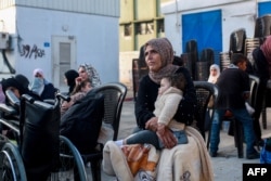 Seorang perempuan menggendong bayi saat mereka menunggu untuk berangkat bersama konvoi Organisasi Kesehatan Dunia dan Bulan Sabit Merah Palestina di Khan Yunis, selatan Gaza. (Foto: AFP)