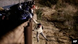 Seorang migran melompati pagar pembatas untuk masuk ke wilayah San Diego, California, AS, dari Tijuana, Meksiko, pada 1 Januari 2019. (Foto: AP/Daniel Ochoa de Olza) 