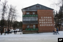 People walk past a house with a Soviet-era slogan that reads "Glory to the Party, Motherland and People!" in the village of Kedrovoye, Russia, Feb. 15, 2018.