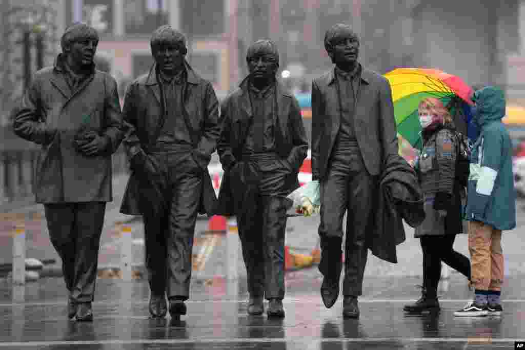 People wearing face masks stand near a statue of The Beatles in Liverpool, England.