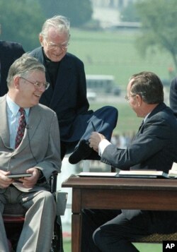 The Rev. Harold H. Wilke, top left, accepts a pen from President George Bush with his left foot, after Bush signed into law the Americans with Disabilities Act of 1990 at a White House South Lawn ceremony July 26, 1990.