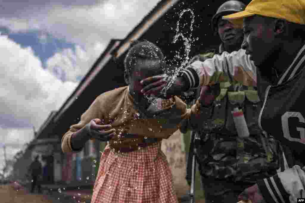 Policemen and residents help a young schoolgirl that inhaled tear gas as the police was trying to hold off a group of supporters of opposition leader while protesting in Kawangware in Nairobi.