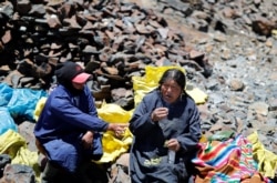 Eva Chura and another woman, who are both 'pallaqueras' known as gold pickers, smoke and drink anise while chewing coca leaves, as part of a ritual for searching for gold performed before a shift, in La Rinconada, the Andes, Peru, October 11, 2019.