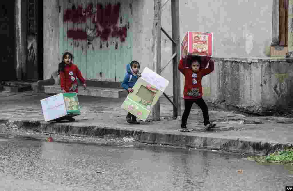 Palestinian girls carry cardboard boxes to shield themselves from the rain, in Rafah, in the Gaza Strip.