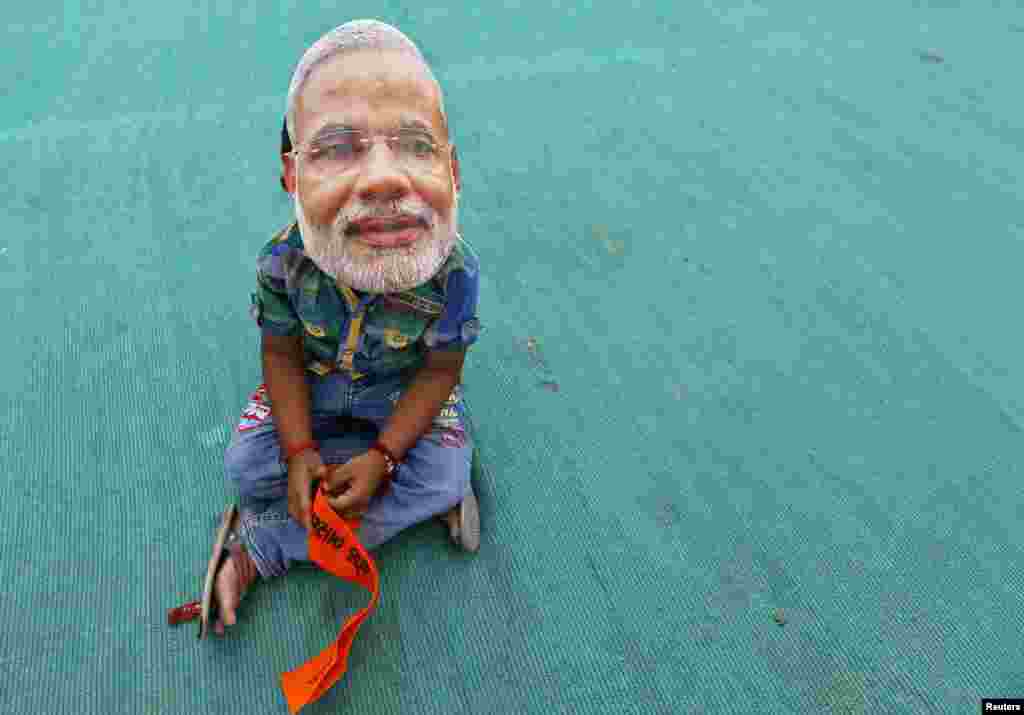 A boy wearing a mask of Hindu nationalist Narendra Modi, prime ministerial candidate for India&#39;s main opposition Bharatiya Janata Party (BJP), sits as he waits for the start of an election campaign rally being addressed by Modi in Kheralu town in the western Indian state of Gujarat.