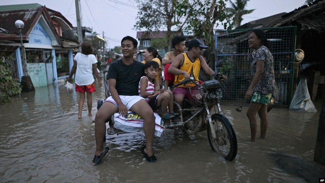 FILE - Residents ride a tricycle in a flooded village after Typhoon Yinxing, locally called Marce, blew past Buguey town, Cagayan province, northern Philippines on Nov. 8, 2024.