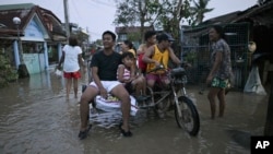 FILE - Residents ride a tricycle in a flooded village after Typhoon Yinxing, locally called Marce, blew past Buguey town, Cagayan province, northern Philippines on Nov. 8, 2024.