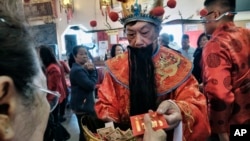 Un hombre vestido con ropa tradicional china entrega una ofrenda a un visitante al tempo Thien Hau en la sección de Chinatown en Los Ángeles, California, el 16 de febrero de 2018.