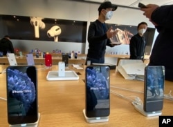 FILE - Staff chats with customers at an apple store in Beijing, Feb. 19. Factories that make the world's smartphones, toys and other goods are struggling to reopen after a virus outbreak idled China's economy.