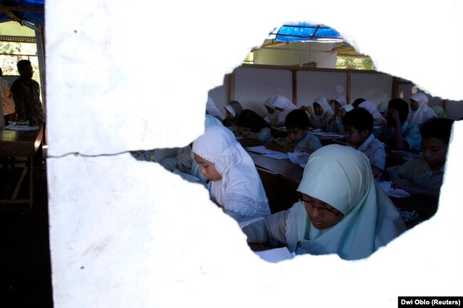 Siswa SMP terlihat melalui lubang di dinding saat mengikuti pembelajaran di gedung sekolah sementara di Bantul, Yogyakarta, 25 Mei 2007. (Foto: Ilustrasi/REUTERS/Dwi Oblo)