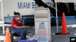 A poll worker wears personal protective equipment as she monitors a ballot drop box for mail-in ballots outside of a polling station during early voting, in Miami Beach, Florida. Aug. 7, 2020.