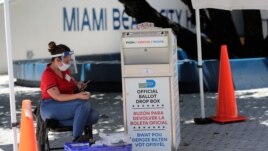 FILE - A poll worker wears personal protective equipment as she monitors a ballot drop box for mail-in ballots outside of a polling station during early voting, in Miami Beach, Florida. Aug. 7, 2020.