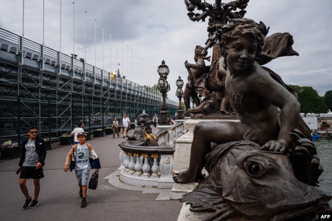 Pedestrians walk past the construction site at the Pont Alexandre III with ongoing works for the 2024 Paris Olympic Games in Paris on July 1, 2024. (Photo by Dimitar DILKOFF / AFP)