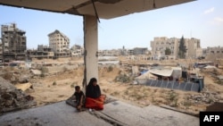 Sebuah keluarga Palestina duduk di sisa-sisa rumah mereka yang rusak akibat pengeboman Israel sebelumnya, ketika beberapa warga kembali ke kota Khan Yunis, di Jalur Gaza selatan pada 30 Juni 2024. (Foto: AFP)