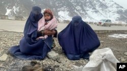 Gulnaz, left, keep her 18-month-old son warm themselves as they wait for alms in the Kabul - Pul-e-Alam highway eastern Afghanistan, Tuesday, Jan. 18, 2022. The Taliban's sweep to power in Afghanistan in August drove billions of dollars in international a