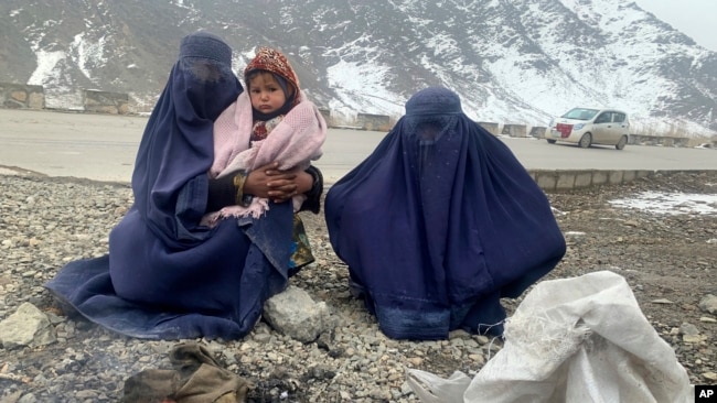 Gulnaz, left, keeps her 18-month-old son warm themselves as they wait for alms in the Kabul - Pul-e-Alam highway eastern Afghanistan, Tuesday, Jan. 18, 2022. (AP Photo/Kathy Gannon)