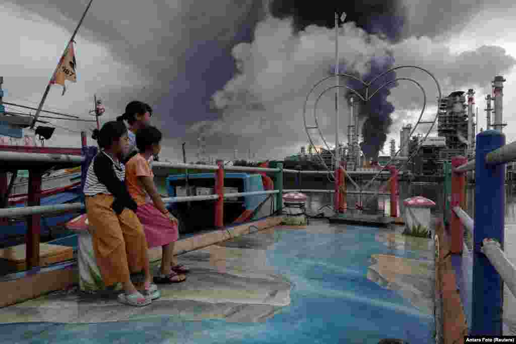 Girls look at black smoke coming from a fire that has broken out at a fuel storage unit at the Pertamina refinery complex in Cilacap, Central Java province, Indonesia.