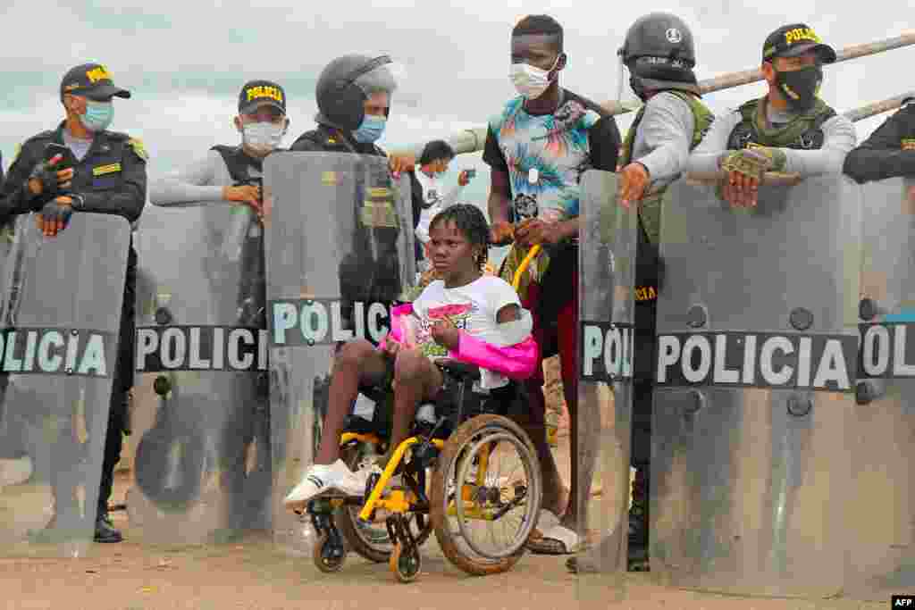 Police open the way to a woman on a wheelchair as a crowd of mix nationality migrants attempt to cross into Peru by the Friendship Bridge on the border with Brazil, 1,600 kilometers southeast of Lima.