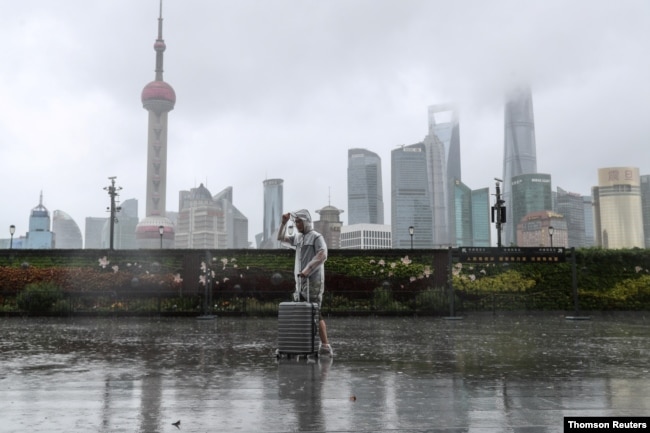 台风“烟花”正在逼近上海，一位男子冒雨走在黄浦江边的外滩。（路透社照片）