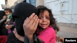 FILE - A girl cries next to her mother covering her face as they flee from an airstrike on an army weapons depot in Yemen's capital Sanaa.