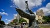 Personas caminan junto a la escultura de una mano que sostiene la estructura de un pozo de petróleo en las afueras de la sede de la estatal PDVSA, en Caracas, el 3 de enero de 2020.