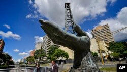 Personas pasan junto a la escultura de una mano que sostiene la estructura de un pozo de petróleo en las afueras de la sede de estatal de Venezuela PDVSA en Caracas. Enero 3, 2020.