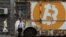 Des gens passent devant un panneau portant le logo de Bitcoin dans une rue d'Erevan, en Arménie, le 9 septembre 2019. (REUTERS/Anton Vaganov)