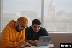 FILE - Iranian cybersecurity experts and members of Certfa Nariman Gharib, left, and Amin Sabeti check their messages as they work from their office in London, Britain, Jan. 7, 2020.