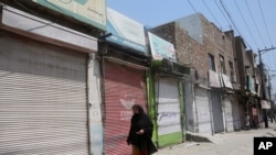 FILE - A woman walks past shops that are closed due to an escalation of cases of the coronavirus in Peshawar, Pakistan, June 17, 2020.