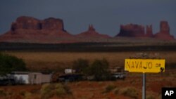 FILE - In this April 30, 2020, photo, a sign marks Navajo Drive as Sentinel Mesa, homes and other structures in Oljato-Monument Valley, Utah on the Navajo Reservation, stand in the distance. 