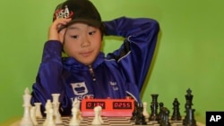Maximillian Lu adjusts his cap as he toys with a chess set during an interview, Nov. 16, 2015, in Armonk, N.Y. The 10-year-old recently became the youngest chess master ever in the United States.