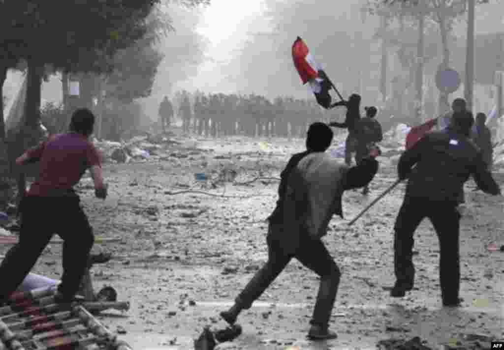 Egyptian protesters threw rocks and firebombs at military police as another waves a national flag during clashes near Cairo's downtown Tahrir Square, Egypt Friday, Dec. 16, 2011. Activists say the clashes began after soldiers severely beat a young man wh