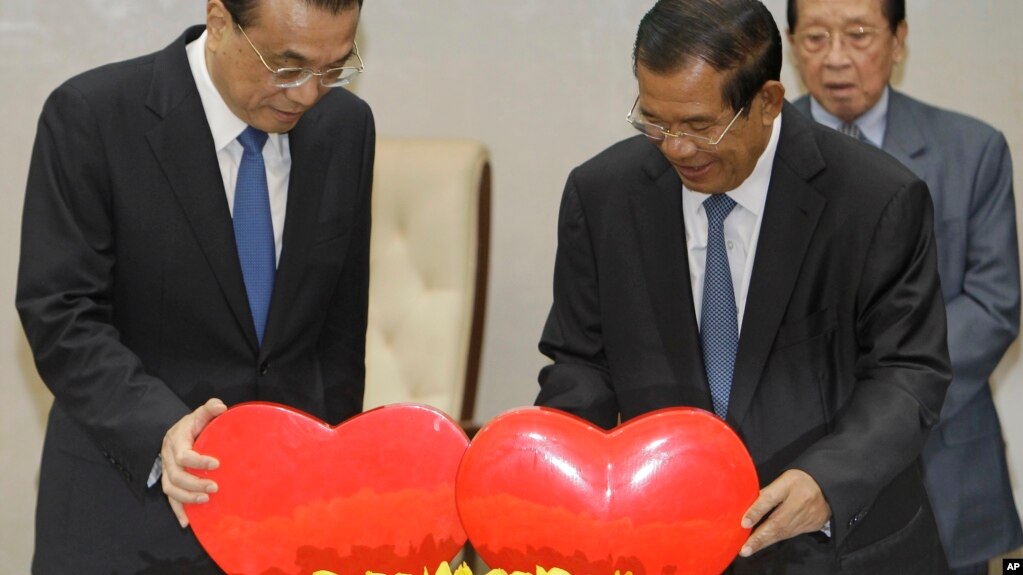 China's Premier Li Keqiang, left, pulls a symbol of China-Cambodia Heart Journey, together with his Cambodian counterpart Hun Sen, center, during a signing ceremony at Peace Palace in Phnom Penh, Cambodia, Thursday, Jan. 11, 2018. Cambodia and China on Thursday signed nearly 20 agreements worth several billion dollars to develop the impoverished Southeast Asian country's infrastructure, agriculture, and healthcare. (AP Photo/Heng Sinith)