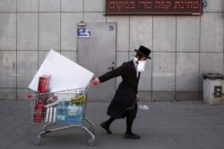 FILE - An ultra-Orthodox Jew wears an improvised protective face mask as he pulls a supermarket cart on a mainly deserted street because of the government's measures to help stop the spread of the coronavirus, in Bnei Brak, a suburb of Tel Aviv.