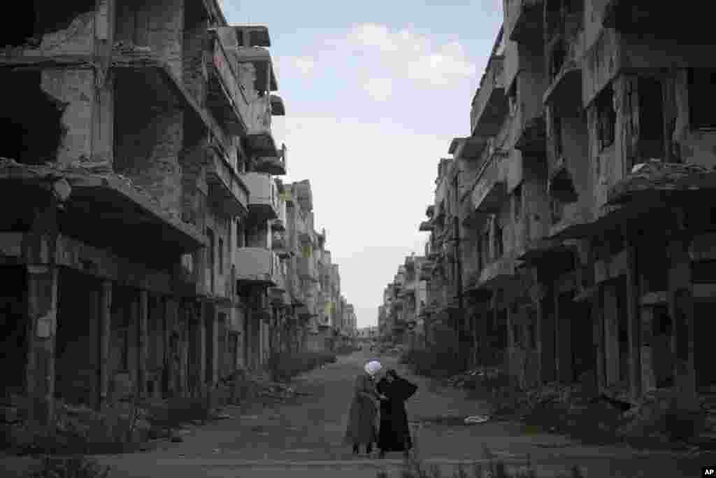 Dua wanita berbincang di jalan yang dikelilingi bangunan-bangunan yang hancur selama perang saudara di distrik Khalidiya di kota Homs, Suriah. (AP)&nbsp;