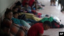 Migrantes venezolanos sentados junto a la pared de un edificio mientras se resguardan de la lluvia, en Matamoros, México, el sábado 13 de mayo de 2023.