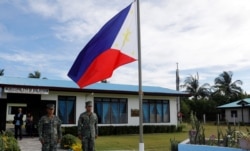 FILE - Filipino soldiers stand at attention near a Philippine flag at Thitu island in disputed South China Sea, April 21, 2017.