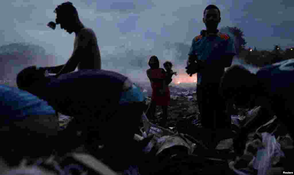 Venezuelan teenager Astrid Prado, 17, who is 7 months pregnant, holds her 1-year-old child Jesuanny as she observes her husband and fellow Venezuelans looking for recyclables at a garbage deposit in Pacaraima, Brazil.