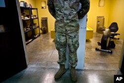 In this June 6, 2018 photo, reviewed by U.S. military officials, a guard stands between two cells, one designed as a library and the other as a gym, in Camp 6 of the Guantanamo Bay detention center, in Cuba.
