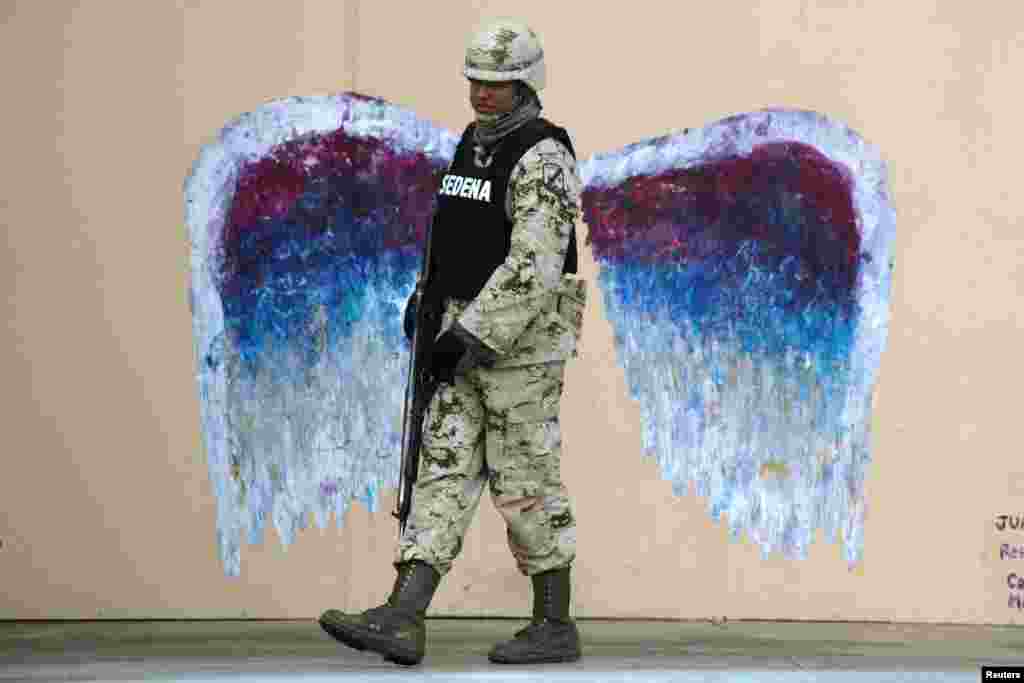 A soldier walks past graffiti depicting angel wings by artist Colette Miller in Ciudad Juarez, Mexico, March 18, 2015.