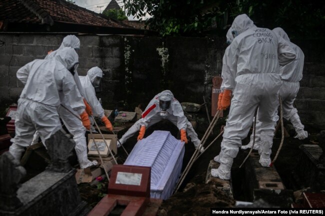Para pegawai dinas pemakaman dengan mengenakan alat pelindung diri (APD) sedang memakamkan jenazah pasien COVID-19 di tempat pemakaman umum di Badran, Yogyakarta, 22 Juni 2021. (Foto: Hendra Nurdiyansyah/Antara Foto via Reuters)