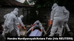 Para pegawai dinas pemakaman dengan mengenakan alat pelindung diri (APD) sedang memakamkan jenazah pasien COVID-19 di tempat pemakaman umum di Badran, Yogyakarta, 22 Juni 2021. (Foto: Hendra Nurdiyansyah/Antara Foto via Reuters)