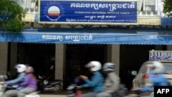 FILE PHOTO - Cambodians ride motorbikes past the headquarters of the Cambodia National Rescue Party (CNRP) in Phnom Penh on October 6, 2017. (Photo by TANG CHHIN SOTHY / AFP)