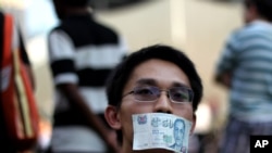 A man covers his mouth with a fifty dollar bill represent the lost of free speech at the Speakers Corner on Saturday, June 8, 2013 in Singapore to protest a new government policy that requires news websites to obtain licenses. The policy that came…