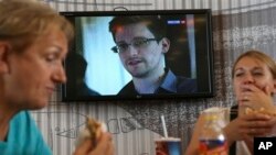 Transit passengers eat at a cafe with a TV screen with a news program showing a report on Edward Snowden, Sheremetyevo airport, Moscow, June 26, 2013.