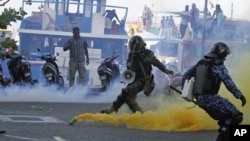 A Maldivian army soldier, left, and policeman take cover as a supporter of Mohamed Nasheed, who resigned Tuesday from his post as Maldivian President, hurls back a tear gas canister thrown during a protest in Male, Maldives, February 8, 2012.