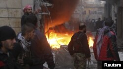 Chiến binh phe nổi dậy đứng cạnh một địa điểm bị cháy, vì đạn pháo của lực lượng chính phủ, trong thành phố Aleppo của Syia, 3/1/13