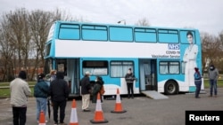 People queue outside a bus modified into a mobile vaccination centre for the coronavirus disease (COVID-19), in Thamesmead, London, Britain, Feb. 14, 2021. 