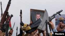 Seorang pengunjuk rasa memegang poster pemimpin Houthi Abdul-Malek al-Houthi, sementara lainnya mengangkat senjata dalam aksi mendukung warga Palestina di Jalur Gaza di tengah konflik Israel-Hamas, Sanaa, Yaman, 26 Juli 2024. (Foto: Reuters)